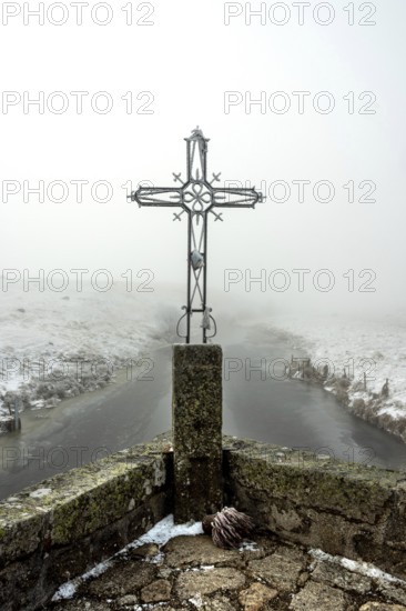 In winter, the Croix du Pont de Marchastel stands proudly amidst a foggy landscape on the Aubrac