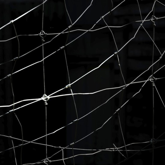 Worn netting stretches across a dark backdrop, showcasing intricate patterns and textures. The play