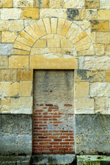 An old stone wall showcases a prominently arched doorway, leading to an unseen area beyond. The