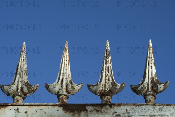 Four rusted metal spikes rise prominently against a vivid blue sky, showcasing weathered details