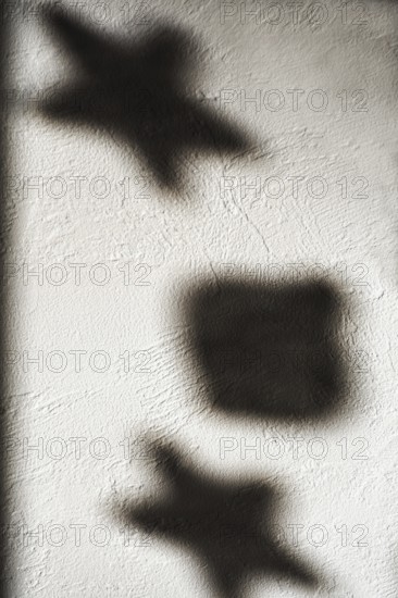 Shapes of stars and a square cast shadows on a textured white wall, illuminated by gentle light.