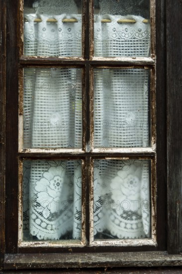 The rustic window displays delicate lace curtains with intricate floral designs, slightly dampened