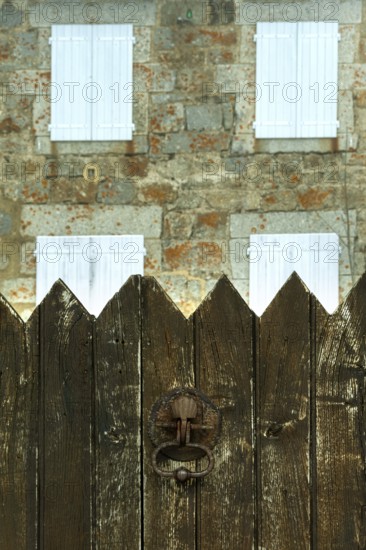 A weathered wooden fence stands in the foreground, with a charming stone house featuring white