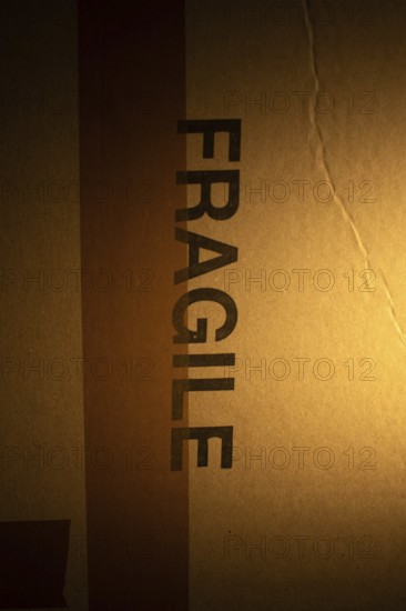A cardboard package with a clear warning label indicating fragile contents is softly illuminated,