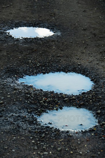 Three puddles on a gravel path mirror the overcast sky, highlighting the damp texture of the ground