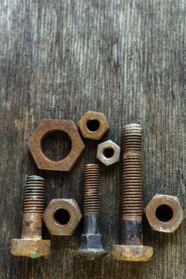 Various sizes and shapes of rusty bolts and nuts are displayed on a weathered wooden surface. Soft