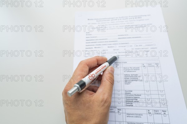 Hand holding a pen while filling out a form on the desk, Care Connect, vaccination kiosk for