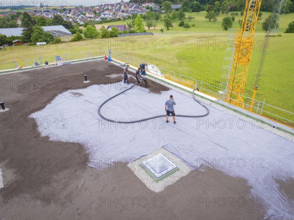 Workers attaching hoses to a roof next to an open field, roof greening, house construction, climate