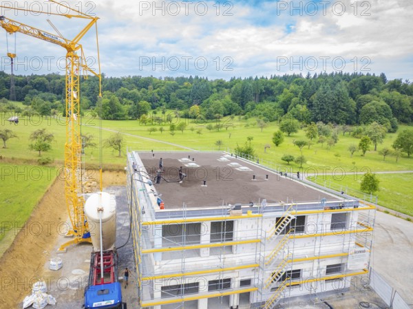A building under construction with a crane and surrounding landscape, green roof, house