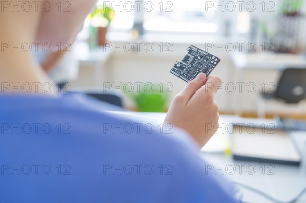 Person holding a circuit board in front of a blurred background with a window view
