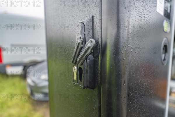 Security lock on a rain-soaked, black housing next to a parked car, installation of a charging