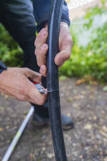 Hands cutting a black cable outdoors with a small cutting tool, assembly of a charging station for
