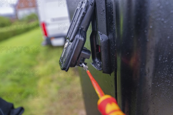 Screwdriver in use on a wet, black housing outdoors, assembly of a charging station for electric