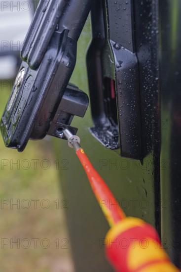 Close-up of a screwdriver attached to a black housing, covered with water droplets, assembly of a