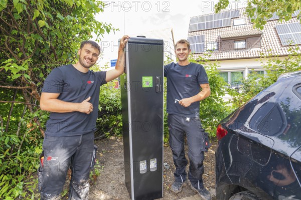 Two technicians pose proudly next to a closed power box outdoors, installing a charging station for