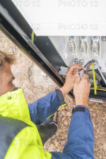 Worker fixing cables with tools in an electrical installation, assembly of a charging station for