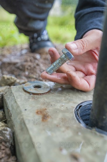 Hand holding a screw for mounting on a concrete base, installation of a charging station for