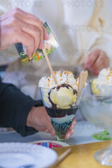 A delicious ice cream sundae with cream and waffle is held by a hand, chocolate sauce visible,