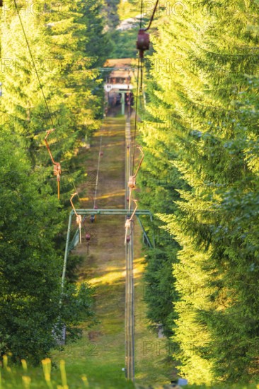 A ski lift moves quietly through a sunny forest surrounded by green trees, Retro Freizeitpark