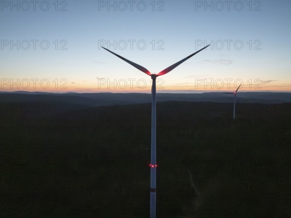 A wind turbine in front of a colourful evening sky with the silhouette in the darkness,
