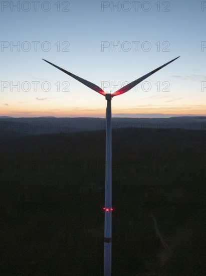 Wind turbine in front of a colourful sunset on the horizon. The sky glows in blue, red and orange,