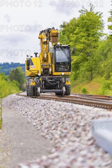 Large yellow machine runs on rails, surrounded by trees and clouds, grinding work on the Hermann
