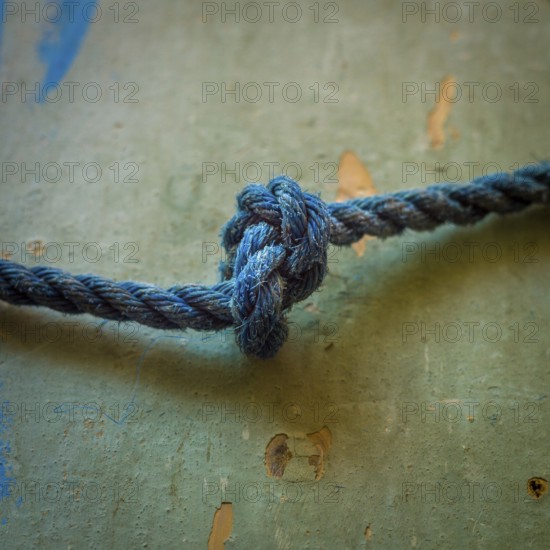 A close-up view reveals an intricately tied blue rope knot resting on a textured surface,