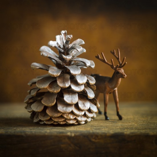 A charming deer figurine stands next to a large pine cone, evoking a cozy winter ambiance. This