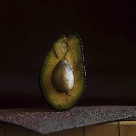 A half avocado is placed on a rough, textured surface, highlighting its smooth, creamy interior and