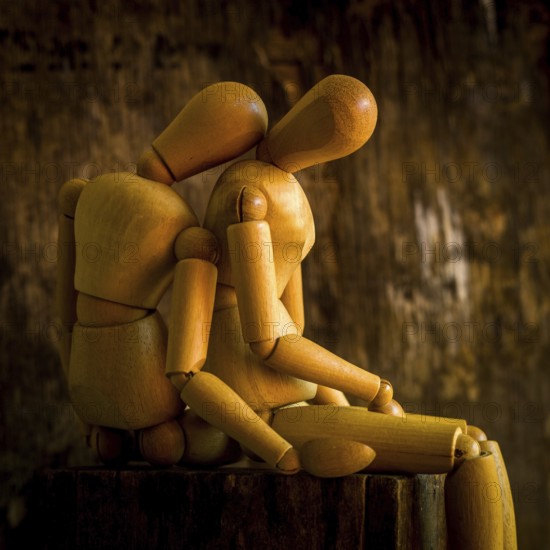 A wooden mannequin is positioned on a rough wooden surface, looking contemplative against a