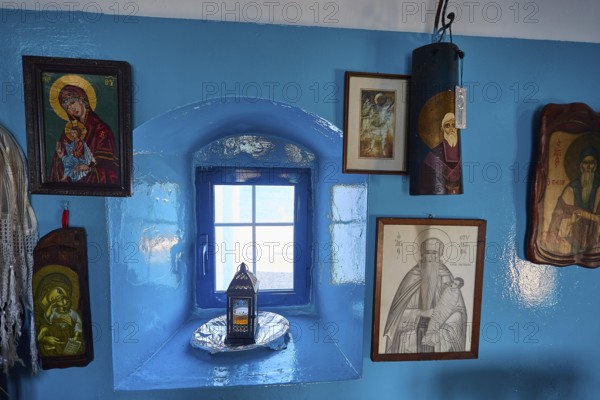 Blue painted wall with various religious pictures around a small window, chapel, church, Agios