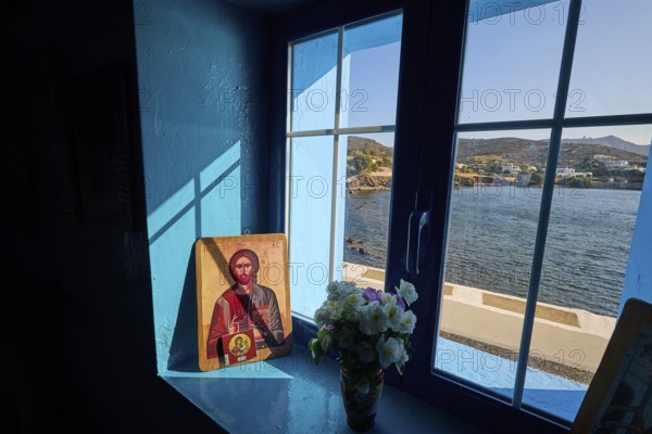 Icon on a windowsill overlooking the sea, surrounded by blue light and a bouquet of flowers,