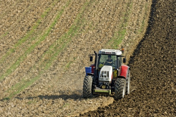 Harvested grain field being turned into a field by Steyr tractor with plough, Hohenpolding, Erding,