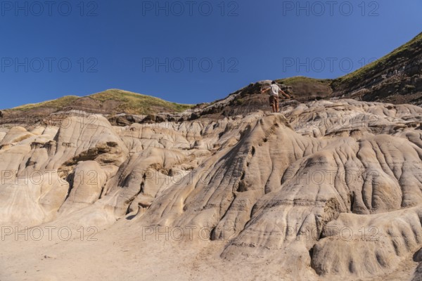 Tourist standing on a hoodoo rock formation, exploring the unique badlands landscape of drumheller,