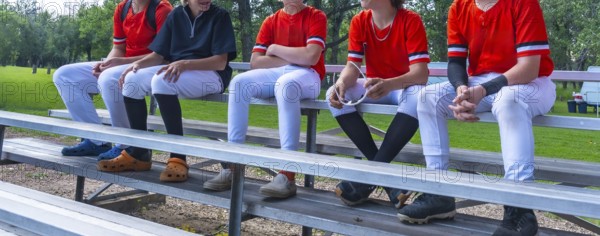 Young baseball players sitting together on bleachers, enjoying camaraderie and conversation after a