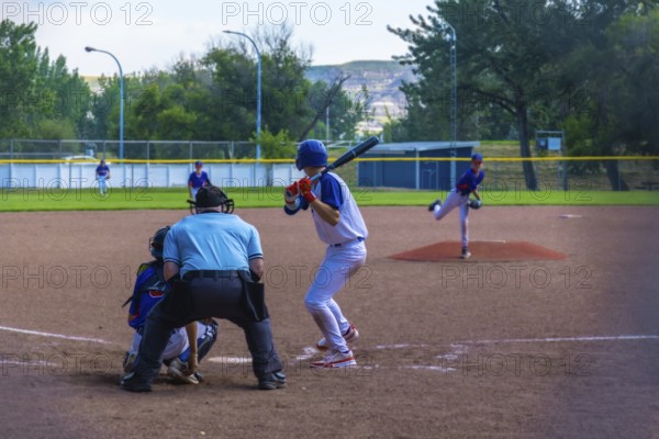 Teenage baseball batter waiting for the pitch while the pitcher is throwing the ball during a sunny
