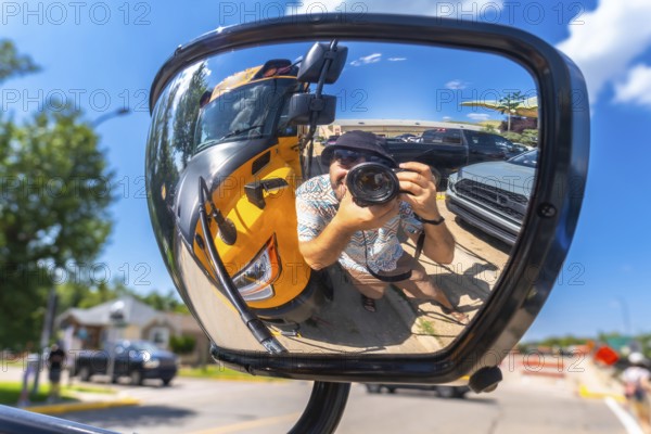 Photographer is taking a selfie reflected in the mirror of a truck, with a yellow school bus and