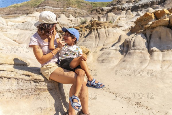 Mother holds her son on her lap, applying sunscreen to his nose during a sunny day exploring the