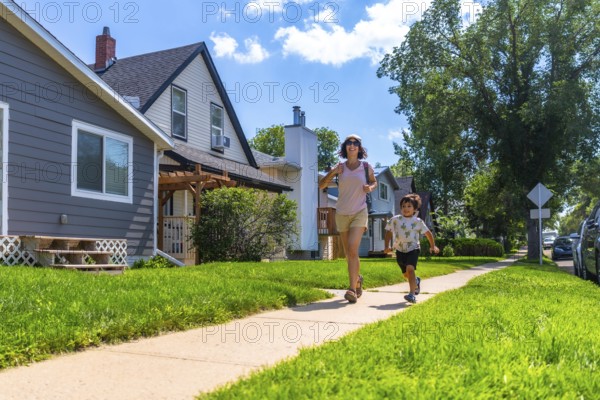 Mother and her young son are running on the sidewalk in a quiet, residential neighborhood on a