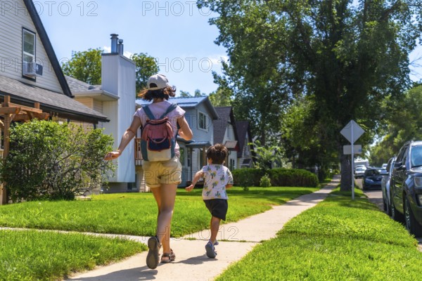 Mother and son running joyfully on the sidewalk in a residential neighborhood of drumheller,