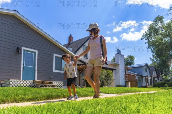 Happy mother and son holding hands and walking on a sidewalk in a residential neighborhood on a