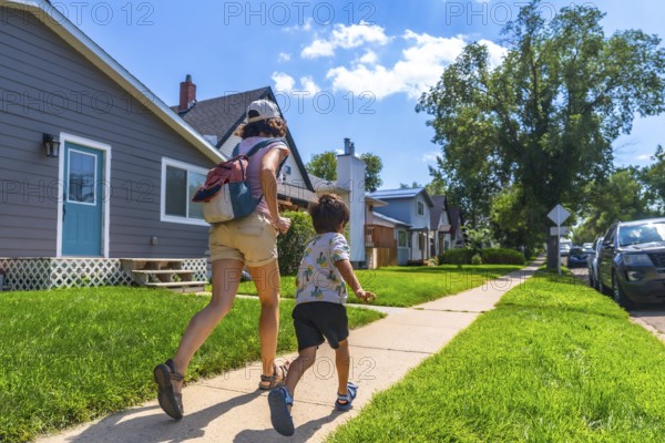 Mother with backpack and her son are running on the sidewalk in a residential area of drumheller,