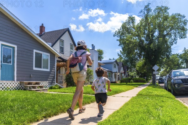 Mother with backpack and her son are running on the sidewalk in a residential neighborhood in