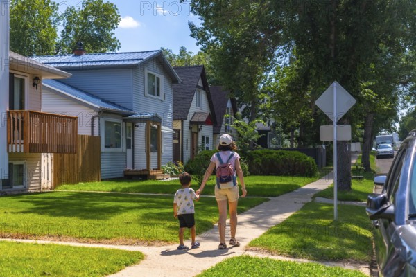 Mother and her young son are enjoying a leisurely stroll along a sidewalk in a quiet residential