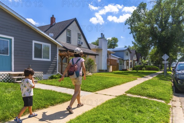 Enjoying a sunny summer day, a mother and her young son stroll along a quiet sidewalk in a charming