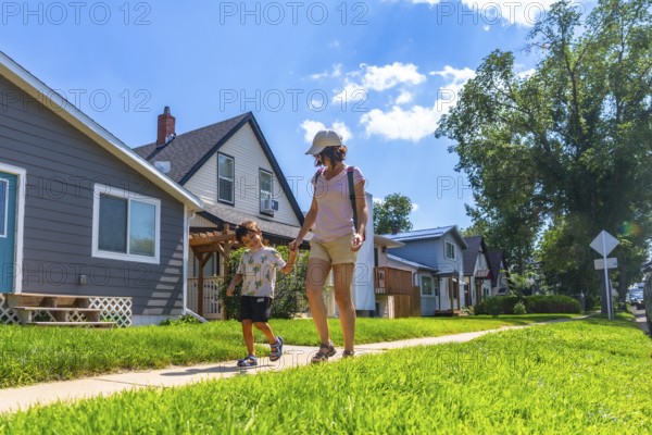 Mother and son walking hand in hand on a sunny day along a sidewalk in a peaceful drumheller
