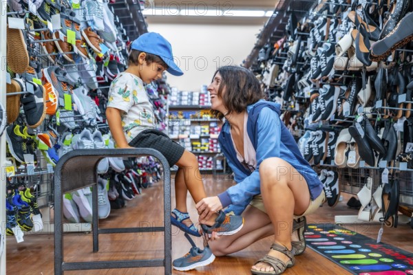 Mother smiling while assisting her son in trying on new shoes at a shoe store, surrounded by a wide