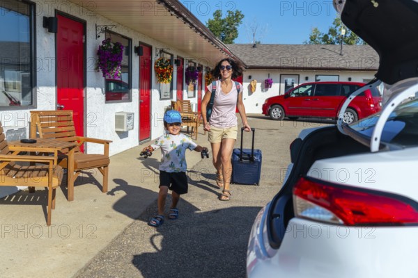 Happy mother pulling a suitcase while her cheerful son runs alongside, playing with toy cars,