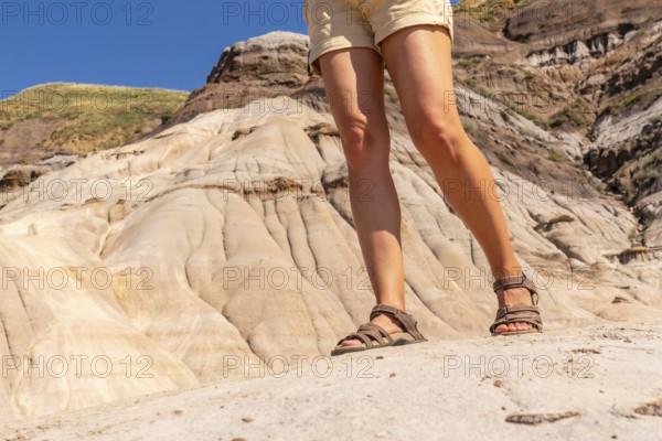 Female tourist wearing hiking sandals standing on the edge of a hoodoo in drumheller, alberta,