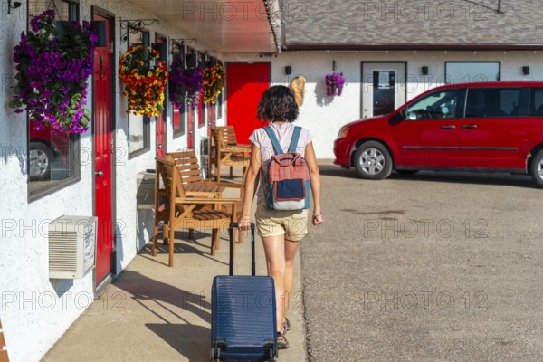 Female tourist walking towards her room at a roadside motel, pulling rolling luggage and wearing a